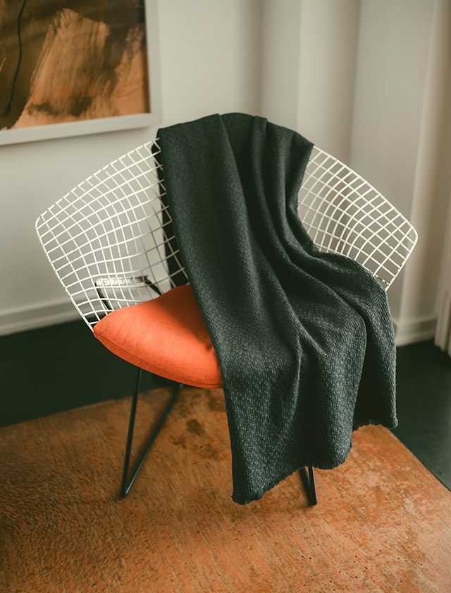 Die OLO Wolldecken von Lapuan Kankurit vereinen hochwertige Naturmaterialien mit zeitlosem skandinavischem Design. Die schwarze OLO Wolldecke wurde hier elegant über einem Bertoia Diamond Chair drapiert.