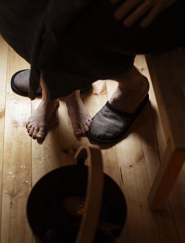 Onni Saunaschuhe von Lapuan Kankurit in Black Leinen neben Saunaeimer auf Holzfußboden