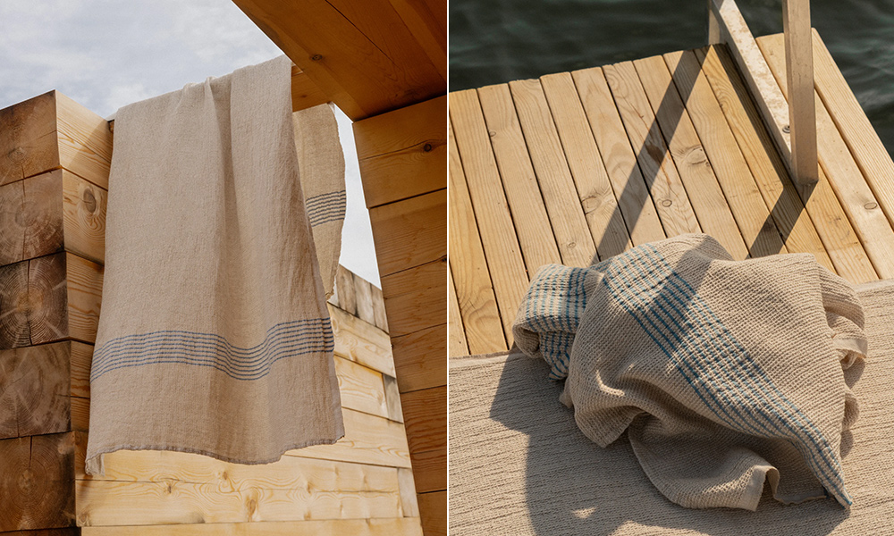 PURO Duschtuch & Saunatuch aus Leinen–Tencel–Baumwolle in Natur mit dezenten blauen Streifen – Waffelstruktur, hängt an Holzsauna und liegt auf Steg am Wasser.