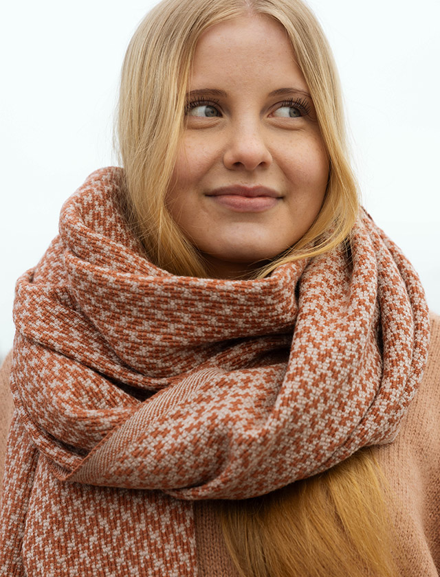 Der Salla Schal von Lapuan Kankurit aus Finnland zeigt ein feines Hahnentritt-Muster in Beige-Cinnamon. Gefertigt aus weicher Merinowolle, wirkt der Schal angenehm wärmend, leicht und hochwertig. Das Bild zeigt den Schal wärmend um den Hals getragen.