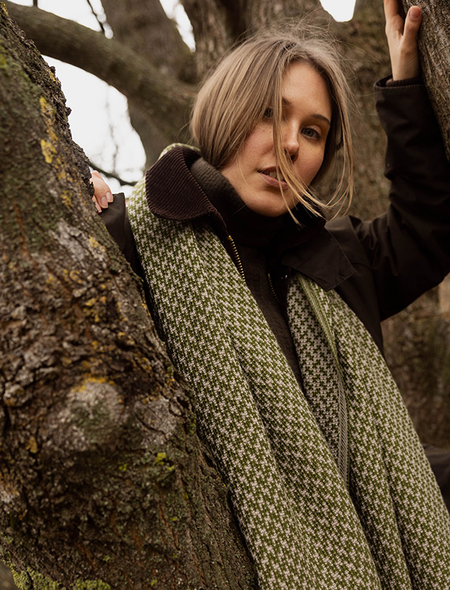 Der Salla Schal von Lapuan Kankurit aus Finnland zeigt ein feines Hahnentritt-Muster in Beige-Olive. Gefertigt aus weicher Merinowolle, wirkt der Schal angenehm wärmend, leicht und hochwertig. Das Bild zeigt den Schal legere um den Hals gehängt – ideal, um die natürliche Struktur, die warme Farbgebung und die nordische Ausstrahlung des Merino-Wollschals zu zeigen.