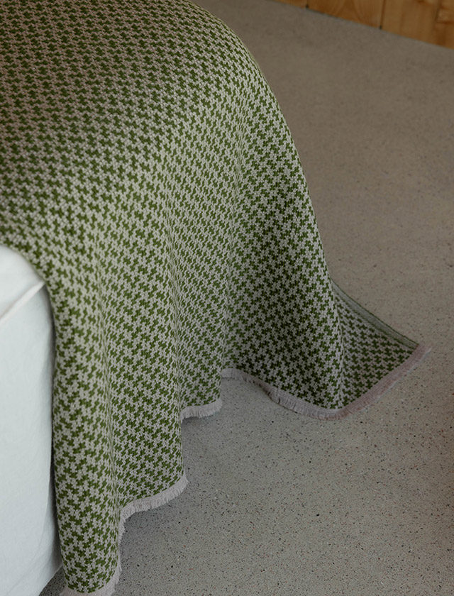 Salla Decke von Lapuan Kankurit aus hochwertiger Merinowolle. Hier liegt die Beige-Olive Decke dekorativ über einer Sitzfläche. Das feine, zweifarbige Hahnentrittmuster verleiht den Wolldecken eine elegante Textur und unterstreicht den skandinavischen Designcharakter. Die Farbpalette umfasst Grün, Rosé, Gelb, Naturweiß und warme Erdtöne. Die weiche Oberfläche der Merinowolle, die hochwertige Verarbeitung und das zeitlose Muster machen die Salla Decke zu einem stilvollen Wohnaccessoire für moderne und klassische Einrichtungen.