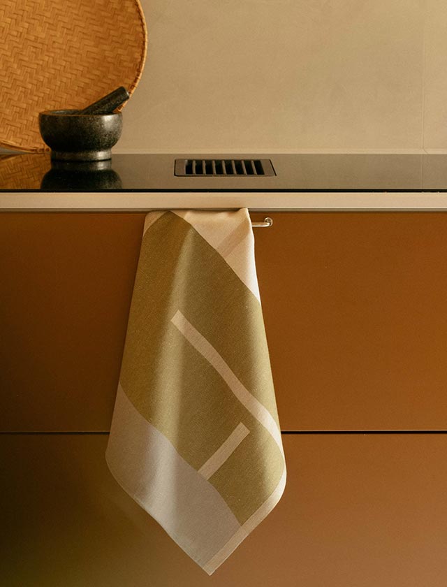 Lapuan Kankurit SUUNTA Handtuch in den Farben Olive, Weiß und Grau. Das skandinavisch inspirierte Design kombiniert grafische Muster mit natürlichen Tönen und hochwertiger Leinen-Baumwoll-Mischung. Das Handtuch ist locker auf einem hellen Untergrund drapiert, was seine Struktur und Weichheit betont. Die dezente Farbgebung und das moderne Muster machen es ideal für minimalistisch eingerichtete Bäder.