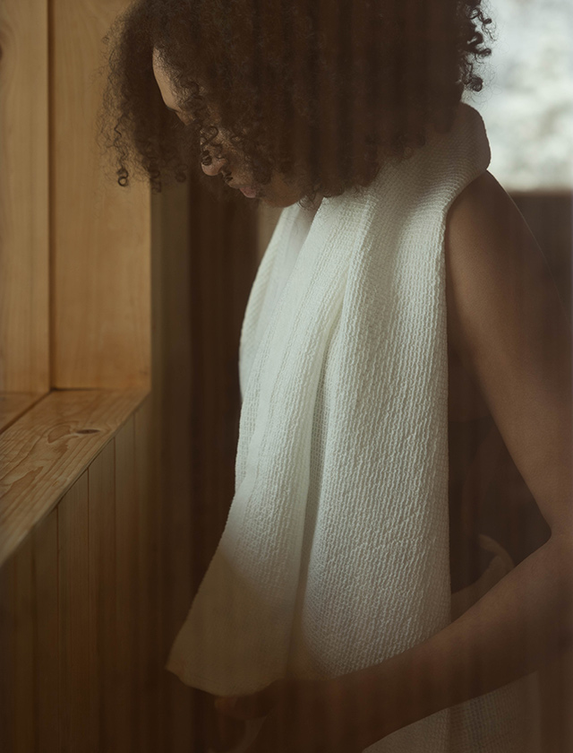 Lapuan Kankurit Terva Handtuch aus Baumwolle in Weiß, locker über die Schultern einer Person in einer holzverkleideten Sauna gelegt.