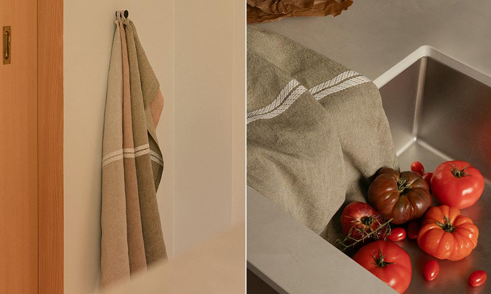 VENLA Küchen- oder Handtuch von Lapuan Kankurit in der Farbe melange olive-white, gestaltet von Designerin Elina Helenius. Links im Bild hängt das Tuch locker an einem Haken an einer hellen Wand, was seine elegante Länge und die dekorative Struktur mit dem gewebten Streifen aus dickerem Garn hervorhebt. Die natürlichen Farbtöne fügen sich harmonisch in das minimalistische skandinavische Interieur ein.