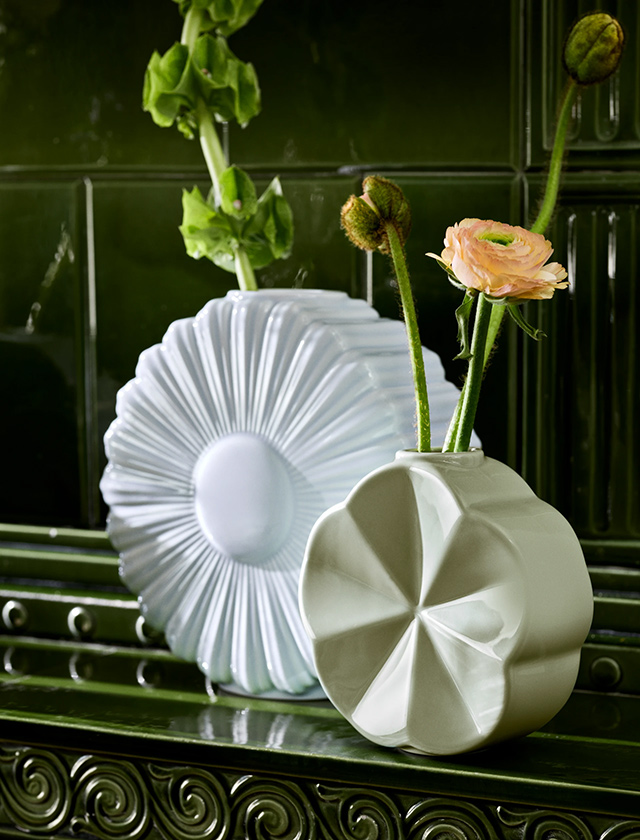 Weiße, facettierte Lyngby Porcelæn Flower Vasen Margerite & Ackerwinde mit zarten Blüten vor dunkelgrüner Fliesenwand.