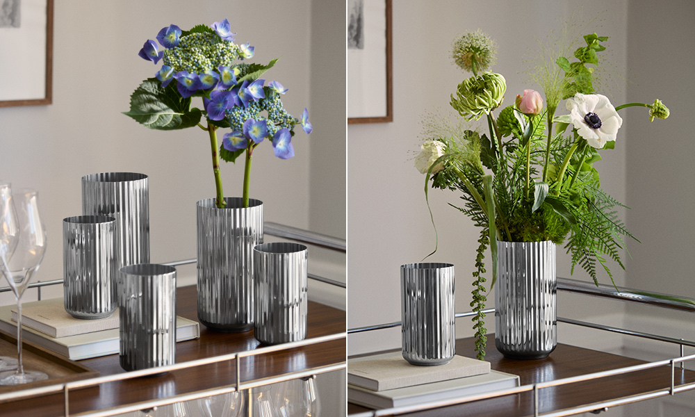 Lyngby Porcelæn Vasen aus Edelstahl mit charakteristischen Rillen, arrangiert mit blauer Hortensie und Blumenstrauß auf einem Sideboard – moderne Neuinterpretation der dänischen Designikone.
