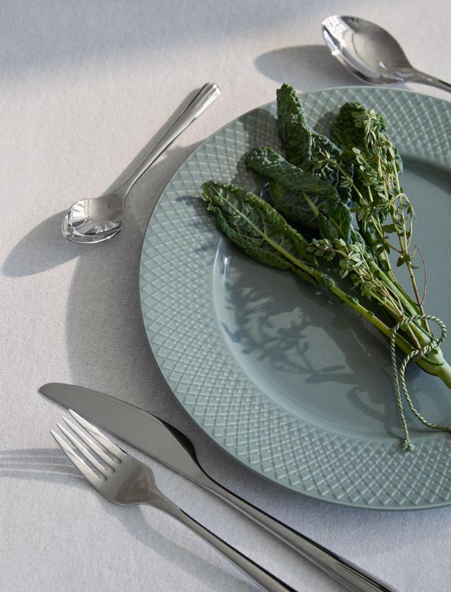 yngby Porcelæn Rhombe Earth Essteller in Moss mit charakteristischem Rhombe-Relief, dekoriert mit frischen Kräutern und Edelstahlbesteck auf einer hell gedeckten Tafel.