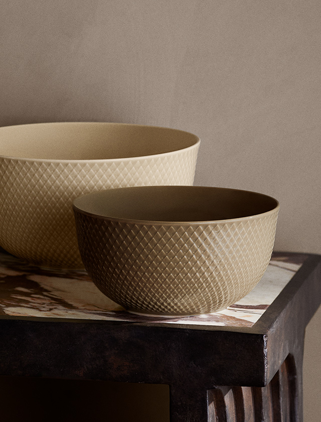 Stilvolle Servierschüsseln der Rhombe Earth-Serie von Lyngby Porcelæn zu sehen. Die größere Schale im Hintergrund ist in einem hellen Beige-Ton gehalten (Farbton "Marble", Ø 22 cm), während die kleinere im Vordergrund in einem warmen Braunton ("Clay", Ø 17,5 cm) erscheint. Beide Schalen zeigen die typische Rhombe-Reliefstruktur, die dem Porzellan eine elegante, strukturierte Oberfläche verleiht.