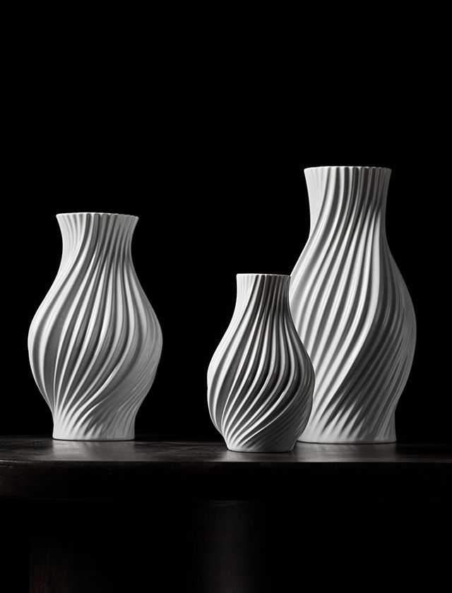 Drei elegante Lyngby Porcelæn Twist Vasen aus weißem Porzellan, kunstvoll in sanft gedrehter Form gestaltet. Die skulpturalen Vasen in verschiedenen Größen vereinen zeitlose Eleganz mit moderner Designästhetik. Vor dunklem Hintergrund kommt die feine Linienstruktur besonders eindrucksvoll zur Geltung – ein stilvolles Wohnaccessoire für Blumenarrangements oder als dekoratives Einzelstück.