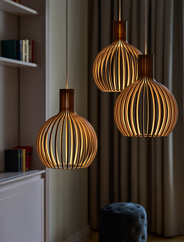 Drei leuchtende Secto Design Octo Tre 4242 Pendelleuchten mit filigranen Holzlamellen, als Gruppe in einem stilvollen Wohnraum arrangiert.