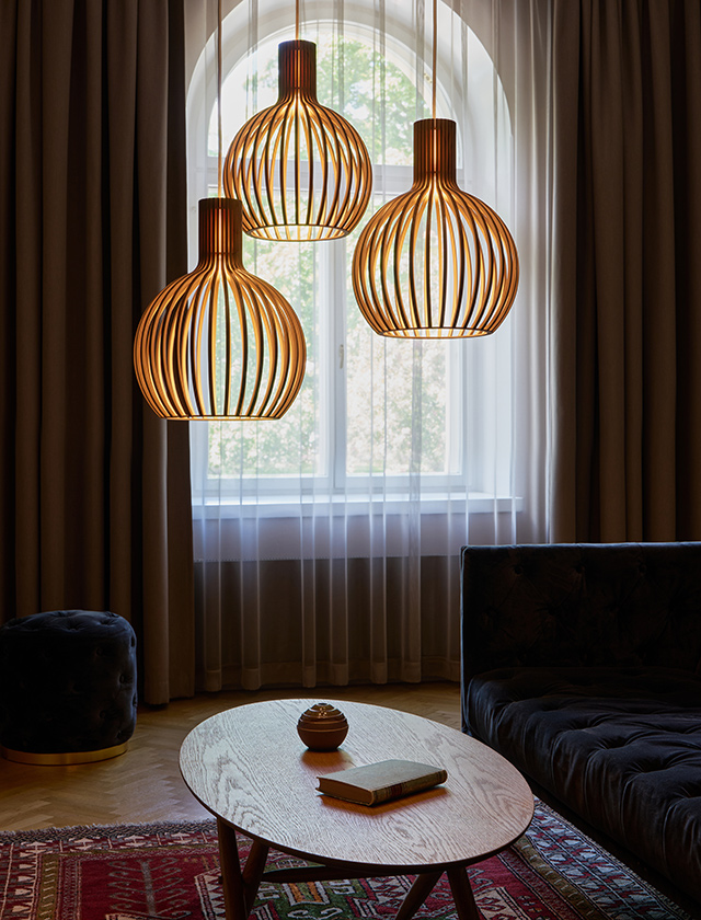 Drei Secto Design Octo Tre 4242 Pendelleuchten aus Birkenholz in einem stilvollen Wohnzimmer vor einem großen Rundbogenfenster.