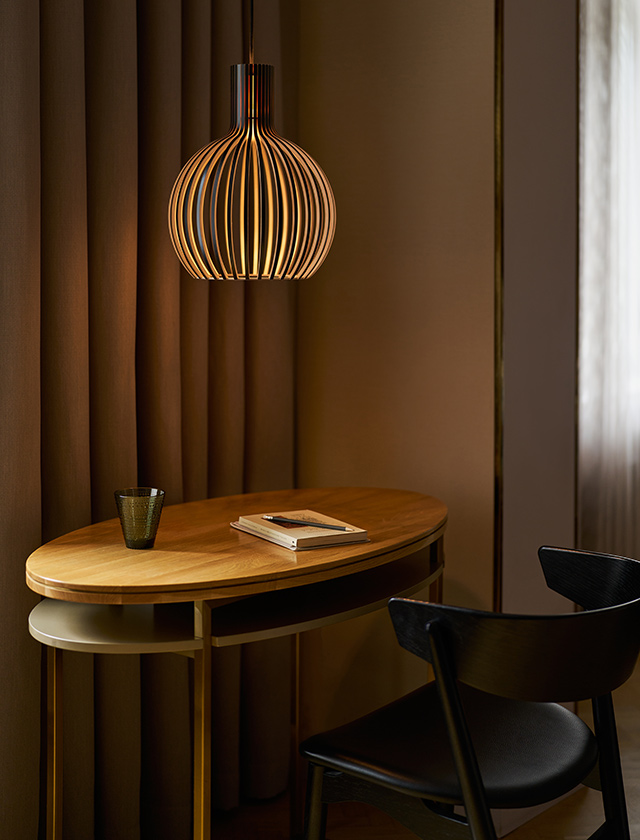 Secto Design Octo Tres 4242 Pendelleuchte schwarz aus Birkenholz über Holztisch, finnische Designerleuchte mit warmem blendfreiem Licht.