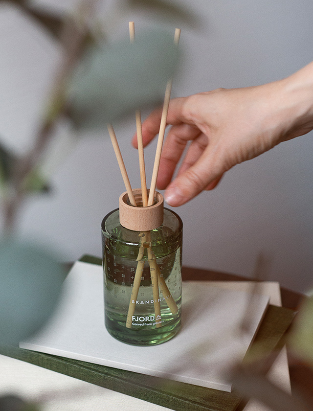 Skandinavisk FJORD Diffuser 200 ml im grünen Glas mit Duftstäbchen auf Büchern in heller Wohnatmosphäre