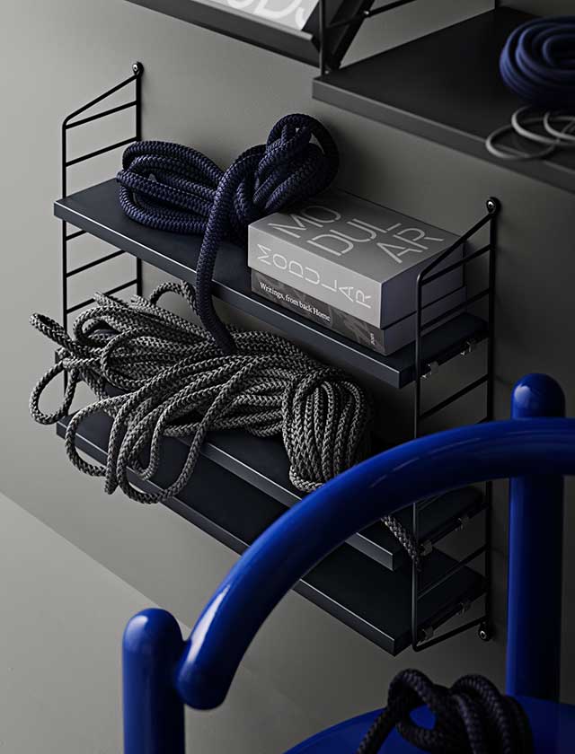 Das Farbschema des Raumes besteht hauptsächlich aus dunklem Grau, Schwarz und Weiß, was eine ruhige, elegante Atmosphäre schafft. Der skandinavisch inspirierte, minimalistische Stil vermittelt Modernität und gleichzeitig eine gemütliche Geborgenheit. Das String-Regal-System erweist sich hier als ideale Wahl für eine aufgeräumte, funktionale Einrichtung, die sich durch ihre schlichte Schönheit und Vielseitigkeit auszeichnet.