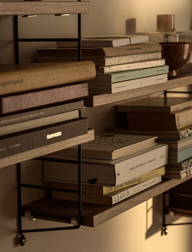 Nahaufnahme des String Pocket Regals von String Furniture in Walnuss und Schwarz mit Büchern, Schalen und dekorativen Objekten auf den Regalböden.