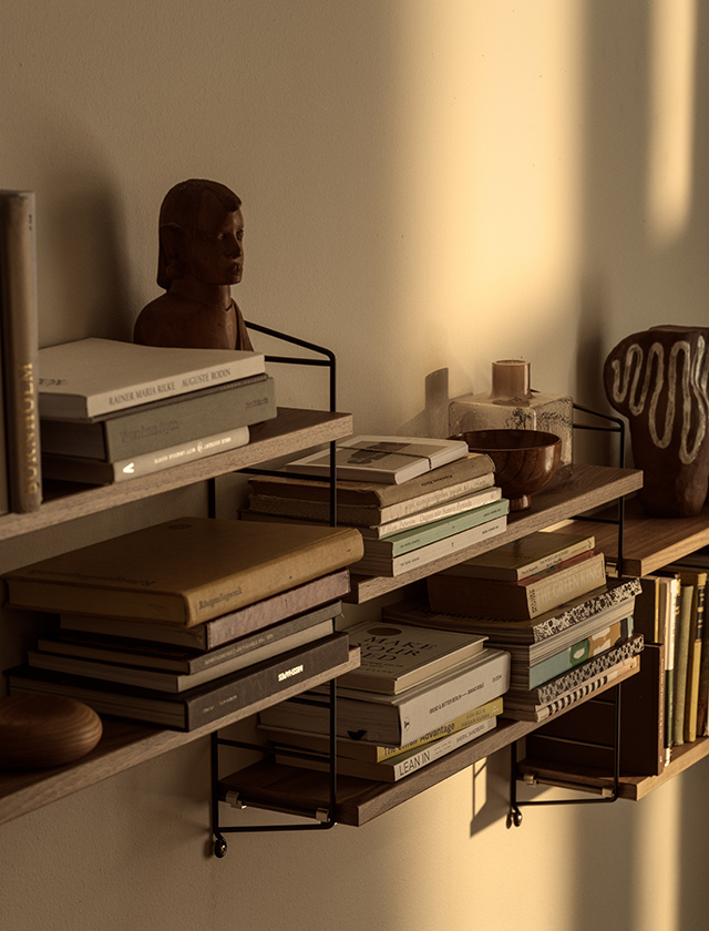 Nahaufnahme des String Pocket Regals von String Furniture in Walnuss und Schwarz mit Büchern, Schalen und dekorativen Objekten auf den Regalböden.