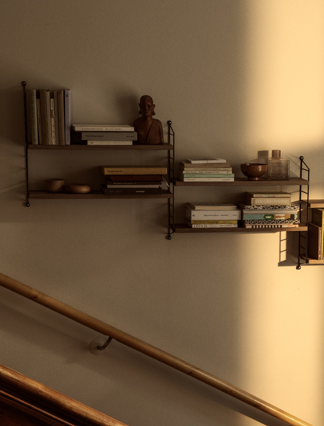 String Pocket Regal von String Furniture in Walnuss und Schwarz, dekoriert mit Büchern und Wohnaccessoires an einer hellen Wand im Treppenhaus.