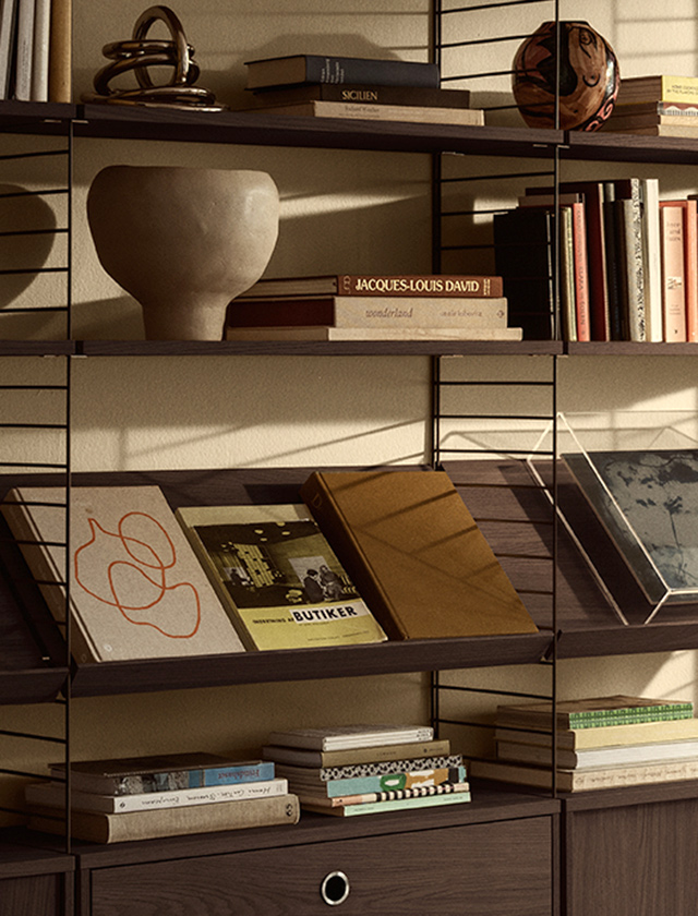 String Regal System mit Magazinablagen und Fachböden in Dark Oak, dunkelbraune Metallleitern, Bücher und Deko im Wohnbereich.