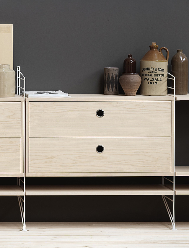 Modernes String Regalsystem mit integriertem Schrankmodul und Schiebetüren aus hochwertigem Eschenholzfurnier. Das skandinavische Design verbindet minimalistischen Stil mit praktischem Stauraum für Wohn- und Arbeitsbereiche.