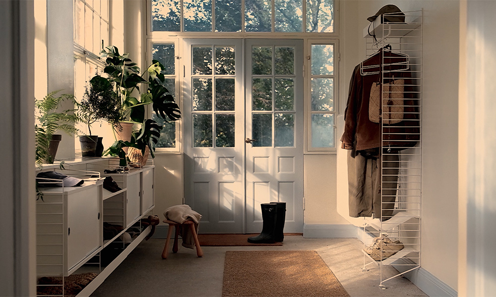 Heller skandinavischer Flur mit weißem String Regalsystem als Garderobe, Schuhablage und Stauraumlösung im Eingangsbereich mit Pflanzen und natürlichem Licht