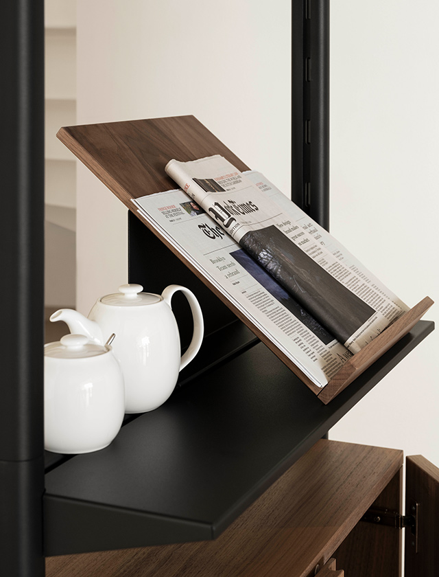 PIRA Regalsystem von String Furniture mit einer Magazinablage aus Walnussholz. Dieses modulare Regalsystem kombiniert schwarze Metallstreben mit edlen Holzelementen, was eine moderne und zugleich elegante Ästhetik schafft.