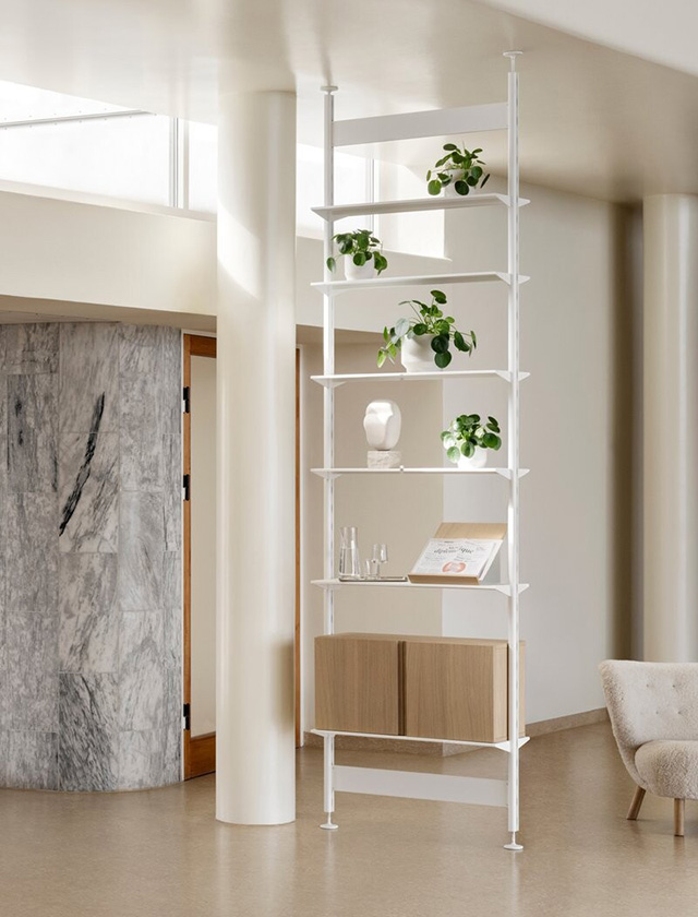 Rira Regalsystem von String Furniture in einer dunklen Variante mit schwarzem Gestell und Walnuss-Schrankelement. Vor einer eindrucksvollen Wendeltreppe wird das Pira G2 hier zur stilvollen Bühne für Designobjekte, Bücher und Keramik. Die dunklen Töne schaffen einen edlen Kontrast zur hellen Architektur und verleihen dem Raum eine ruhige, fast meditative Atmosphäre. Ein idealer Einsatzort: moderne Lounge-, Empfangs- oder Galeriebereiche, in denen klare Linien und Qualität gefragt sind.