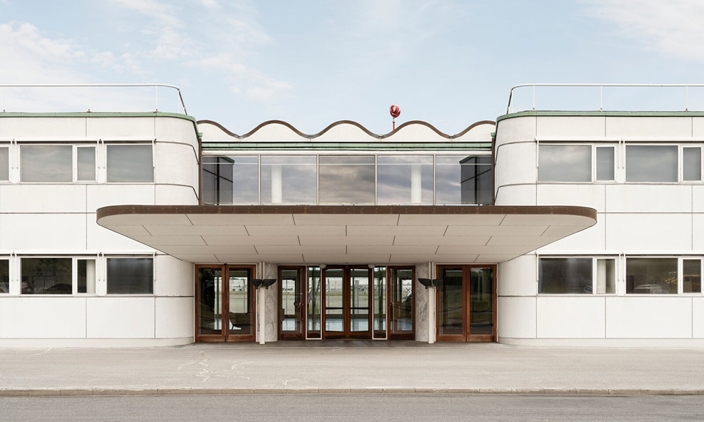 Der Vilhelm Lauritzen Terminal am Flughafen Kopenhagen ist ein architektonisches Juwel der Moderne und ein herausragendes Beispiel für den dänischen Funktionalismus der 1930er Jahre. Entworfen vom renommierten Architekten Vilhelm Lauritzen, besticht das Gebäude durch seine elegante Klarheit, harmonische Proportionen und eine Formsprache, die Technik und Ästhetik auf besondere Weise verbindet. Die helle Fassade mit ihren horizontalen Linien und sanft gerundeten Ecken erinnert an die Gestaltung von Flugzeugen oder Ozeandampfern – typisch für den Geist der Zeit, der Fortschritt und Bewegung in die Architektur übersetzte. Besonders markant ist die wellenförmige Dachlinie, die dem nüchternen Bau eine spielerische Leichtigkeit verleiht.