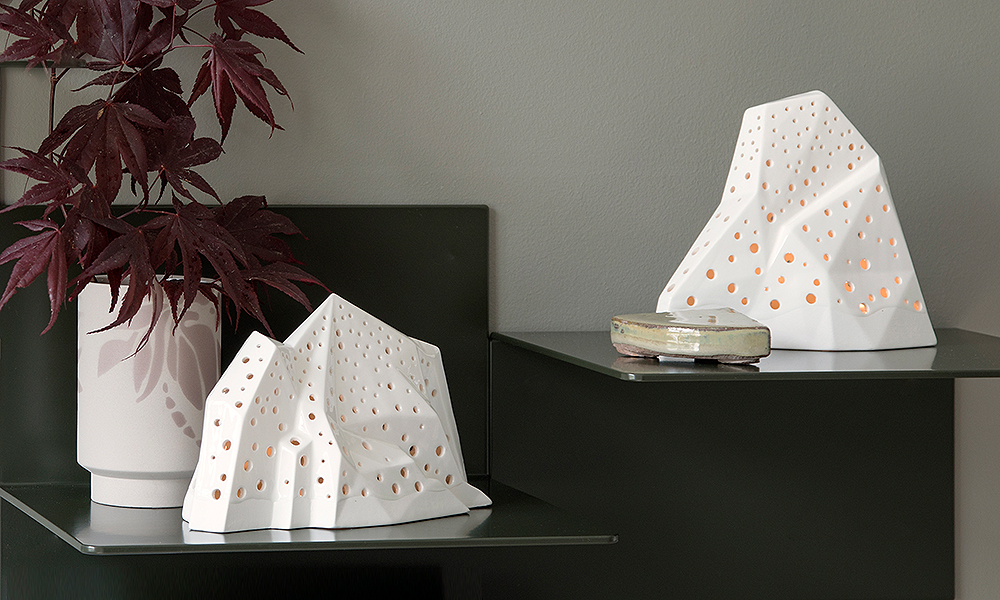 Zwei schneeweiße Nobili Mountain Stimmungslichter und eine Kabell-Vase von Kähler Design. Die schneebedeckten Berge kontrastieren hervorragend mit dem schwarzen Metallregal aus Dänemark. In der rosafarbenen Kabell-Vase ranken Zweige des japanischen Zimmerarhorns.