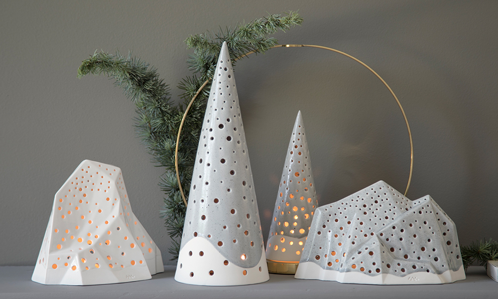 Ein Ensemble bestehend aus vier Stimmungslichtern aus der Nobili-Serie von Kähler Design. Der hohe weiße Berg und der breite, graue Berg sind mit zwei frostgrauen Kegeln kombiniert. Der Reifen im Hintergrund ist von Klong gefertigt.