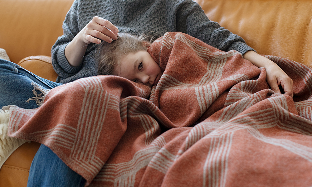 Frau mit Kind kuscheln auf einem Sofa. Eine terrakottafarbene Wolldecke aus der Himmeli-Serie wärmt die Tochter.